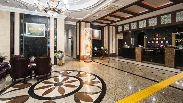 A lobby with a reception desk, seating area, and a decorative column. - Hotel Aura (Ansan)