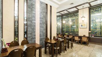 Un restaurante con una barra alargada, varias mesas y sillas. Cuenta con paneles decorativos en la pared y una araña.