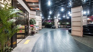 A modern hotel lobby with a curved tiled floor, a staircase, and a row of parked cars. - Hotel Aura (Ansan)