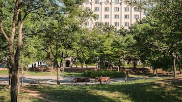 A park with benches and trees, a pathway, and a building in the background.