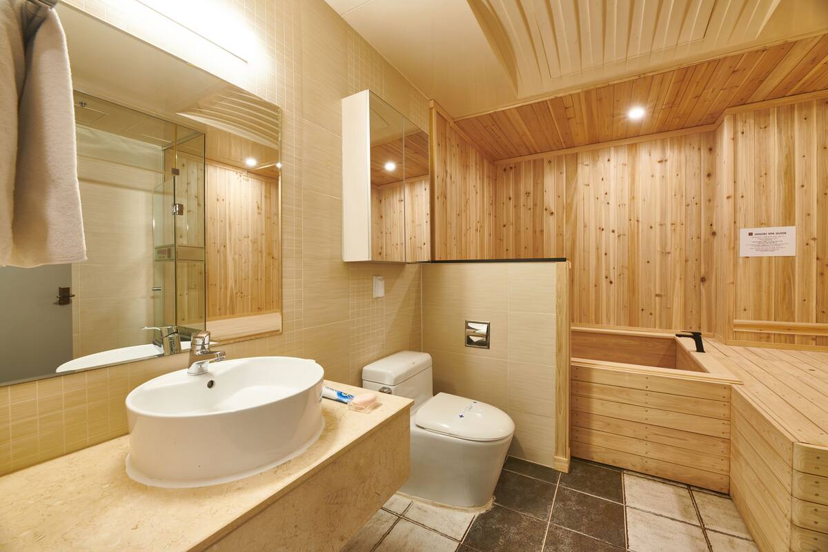 A wooden bathroom with a large sink, toilet, and wooden bathtub.