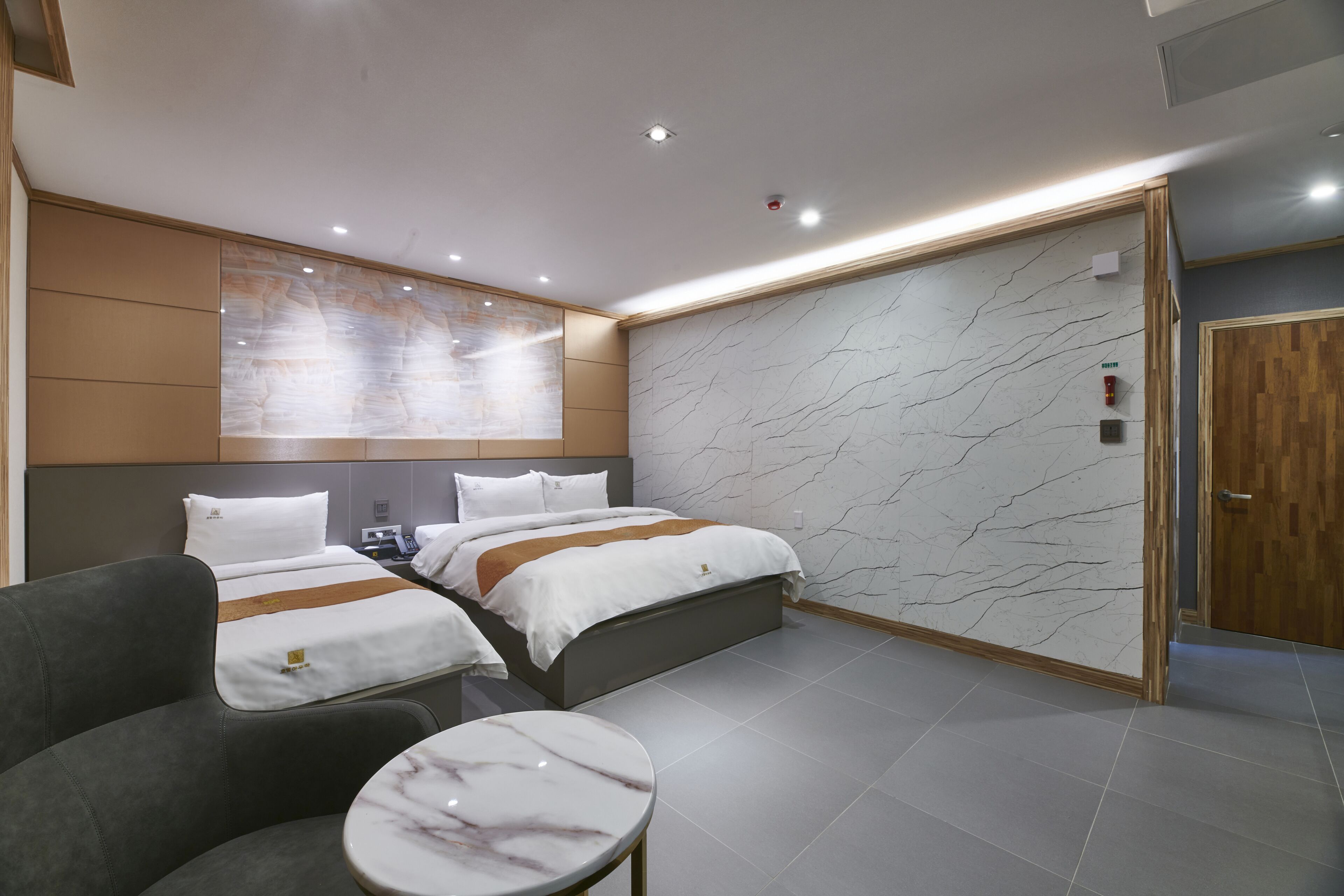 A modern hotel room with two beds, a sofa, a marble table, and a marble-patterned wall.