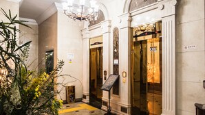 A lobby with a marble floor, a chandelier, and an elevator. - Hotel Aura (Ansan)