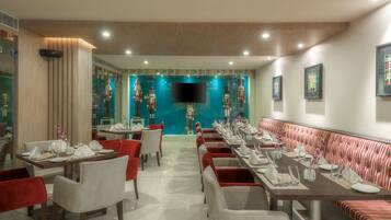 A restaurant with a long dining table, red and white chairs, and a striped bench.