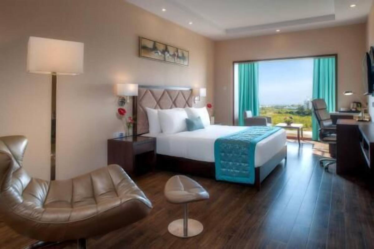 Une chambre d’hôtel avec un lit, un bureau, une chaise, un canapé, une lampe et un tableau au mur.