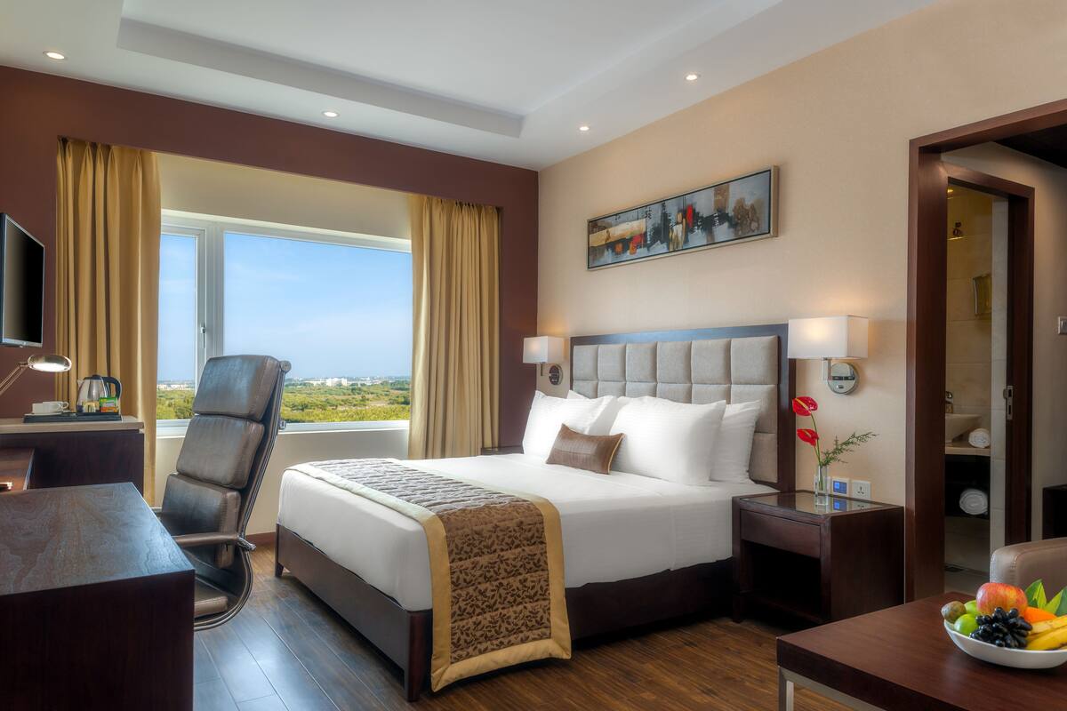 Une chambre d’hôtel avec un grand lit, un bureau avec une chaise, une télévision et une vue sur l’extérieur.
