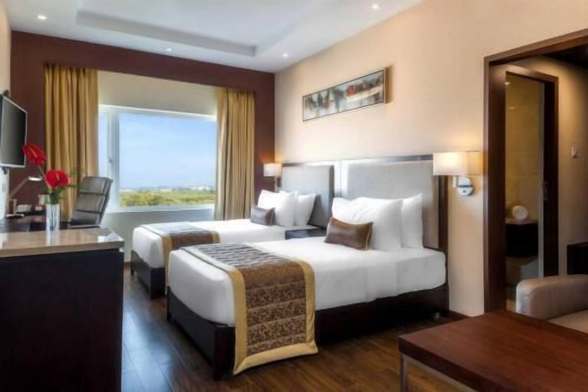 Une chambre d’hôtel avec deux lits, un bureau, une chaise, une télévision et une fenêtre avec des rideaux.