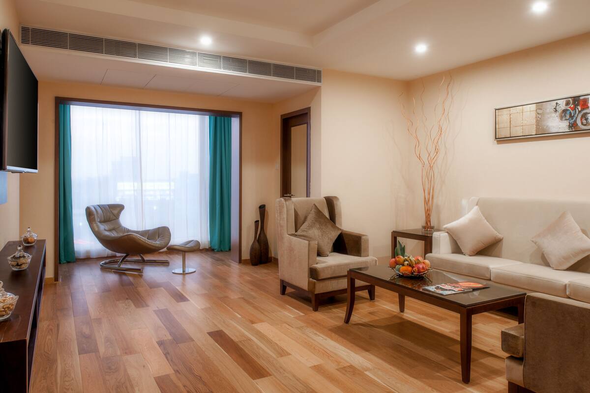 Un salon moderne avec un plancher en bois, un canapé, une table basse, un téléviseur et une grande fenêtre avec des rideaux.