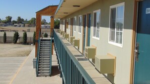 A motel with a covered outdoor staircase leading to a row of rooms. - Corcoran Country Inn (Corcoran)