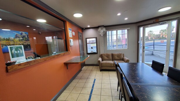 A hotel reception area with a counter, a sofa, and a dining table. - Corcoran Country Inn (Corcoran)