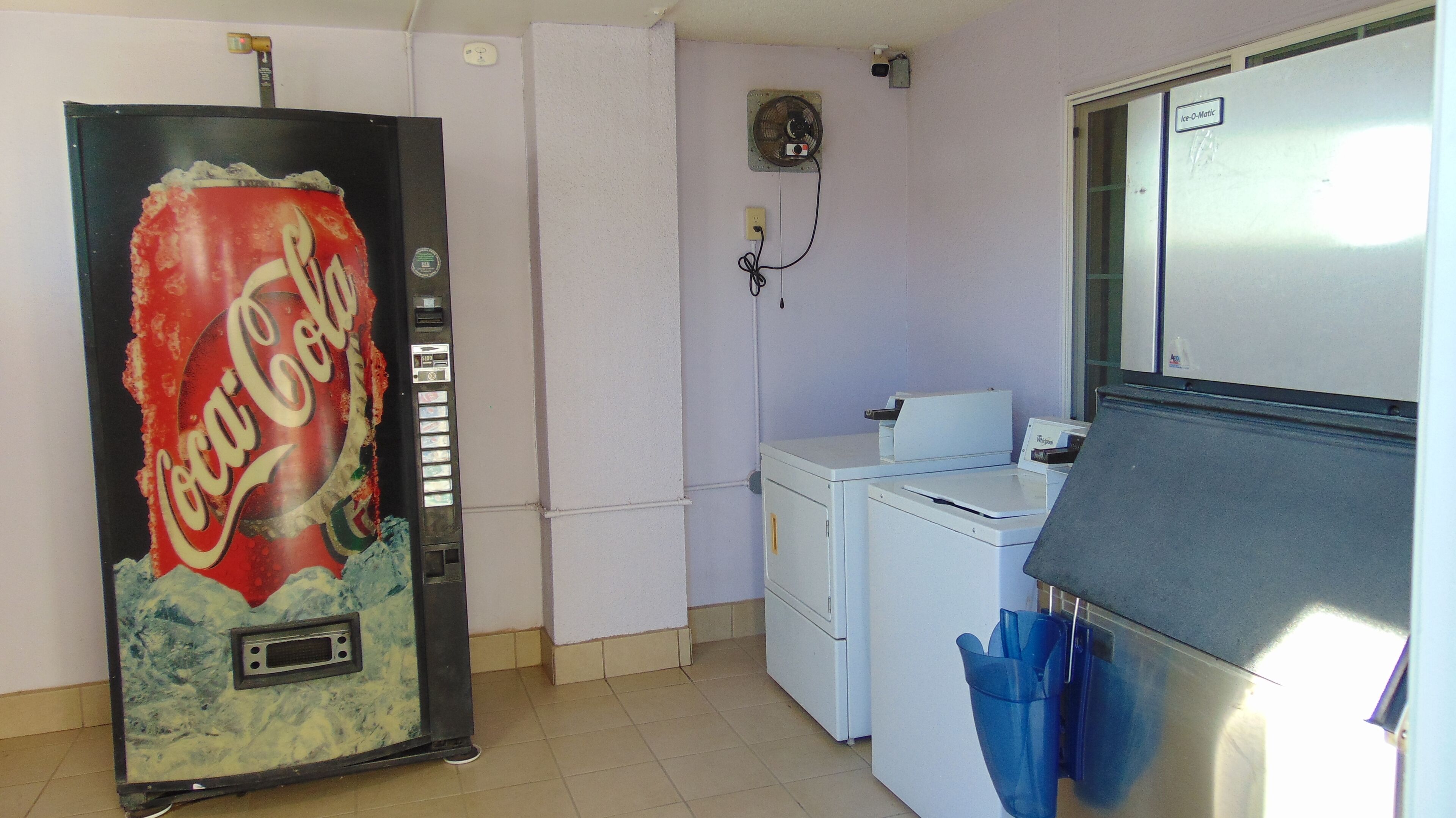 Una cocina con una máquina expendedora de Coca-Cola, una lavadora y un refrigerador.