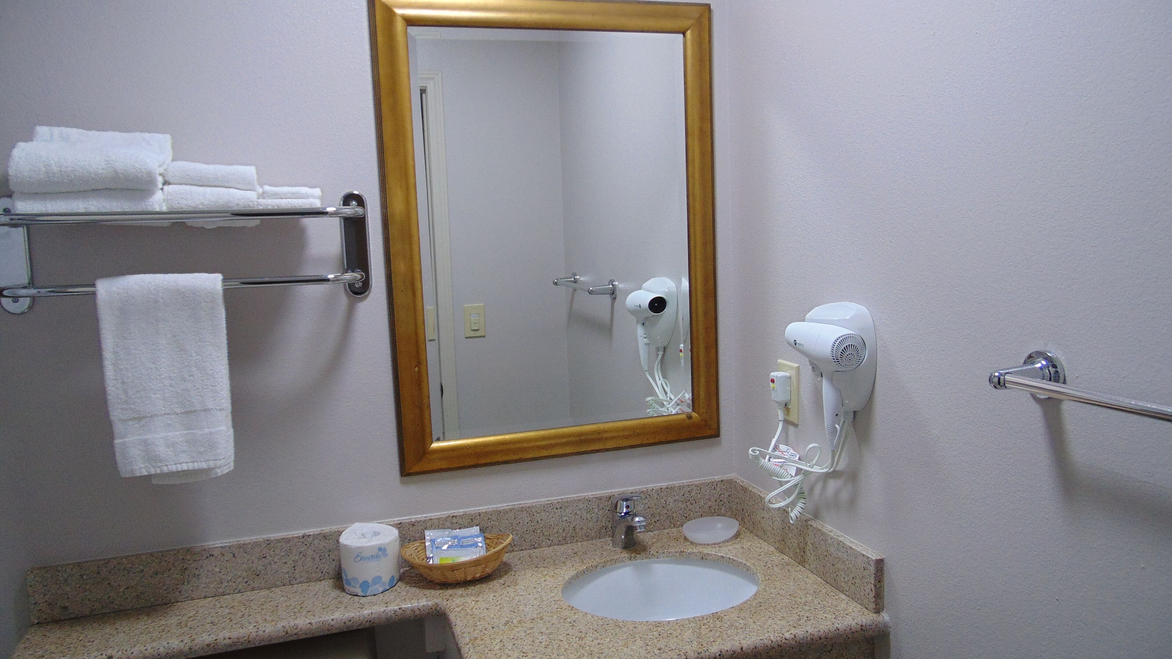 Une salle de bain équipée d’un lavabo, d’un miroir, d’un porte-serviettes et d’un sèche-cheveux.