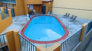An outdoor swimming pool with a red border, surrounded by a concrete deck and metal railings. - Corcoran Country Inn (Corcoran)