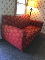 Un sofá rojo con estampado de hojas en una habitación con papel tapiz floral y una lámpara.