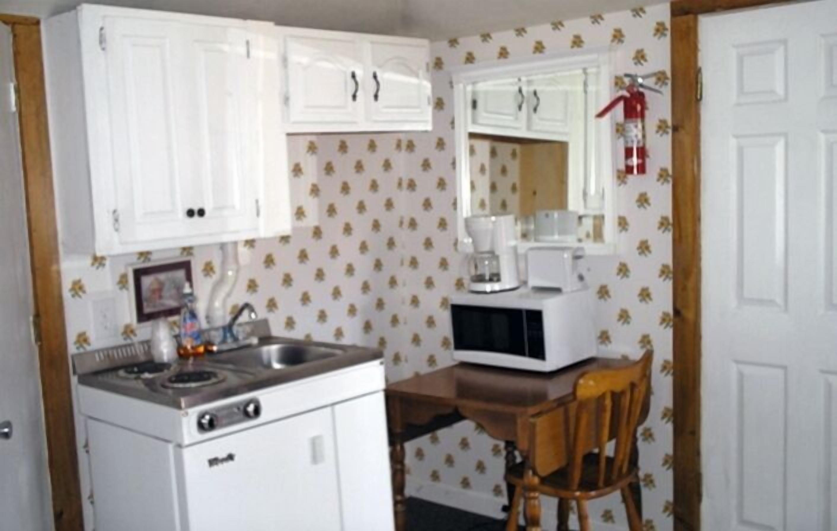 Une cuisine de taille réduite avec des meubles blancs, une cuisinière, un four à micro-ondes et une chaise en bois.
