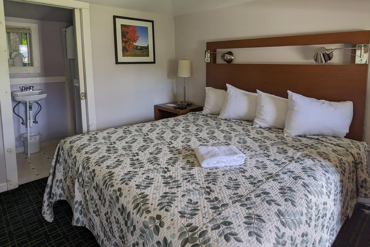 Uma cama bem arrumada com colcha florida, um abajur e um quadro na parede.