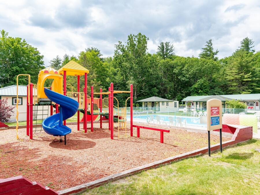A playground with a blue slide, red and yellow play structures, and a fenced swimming pool area.