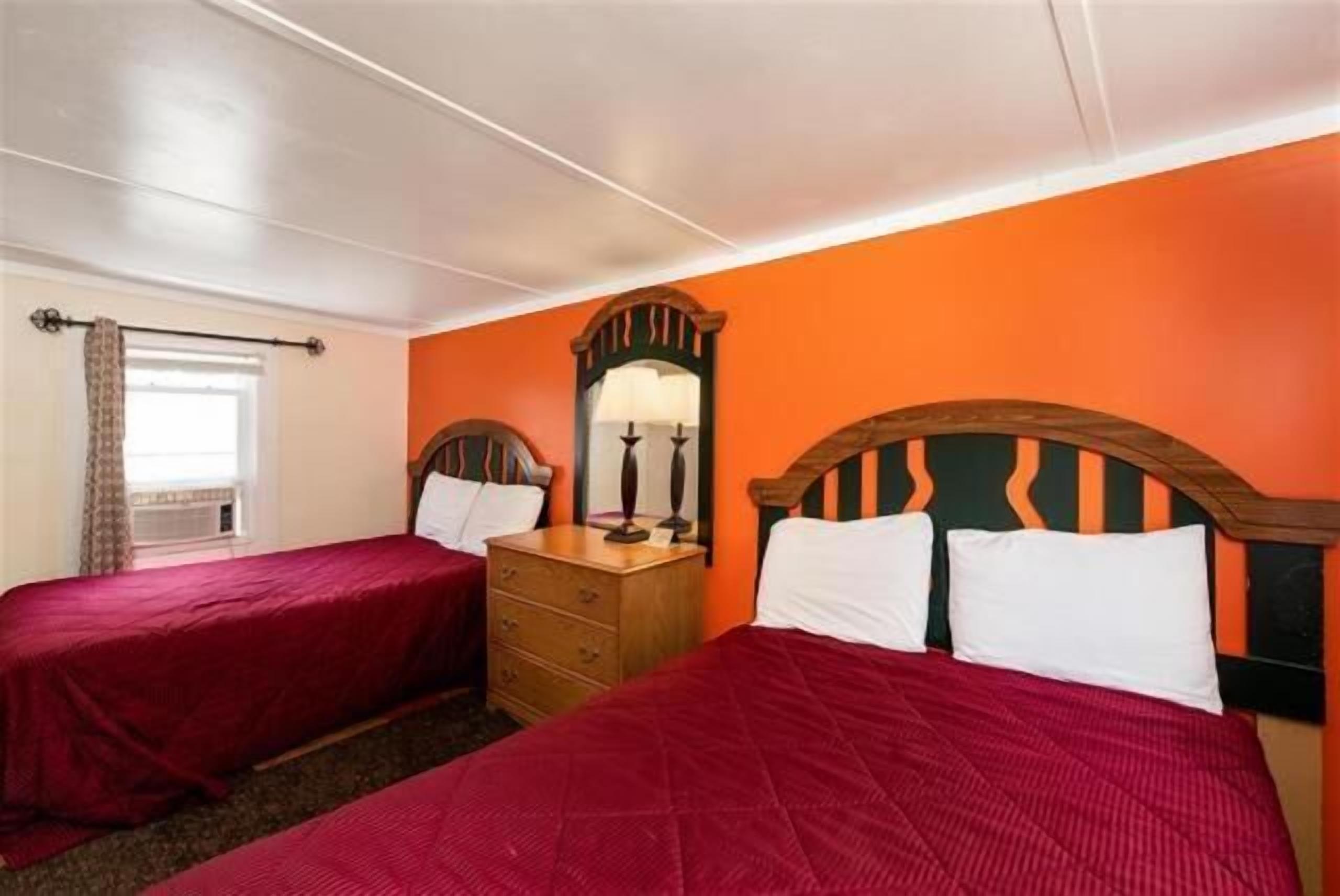 Ein Hotelzimmer mit zwei Einzelbetten, einem hölzernen Schminktisch, einem Spiegel und einer orangefarbenen Wand.