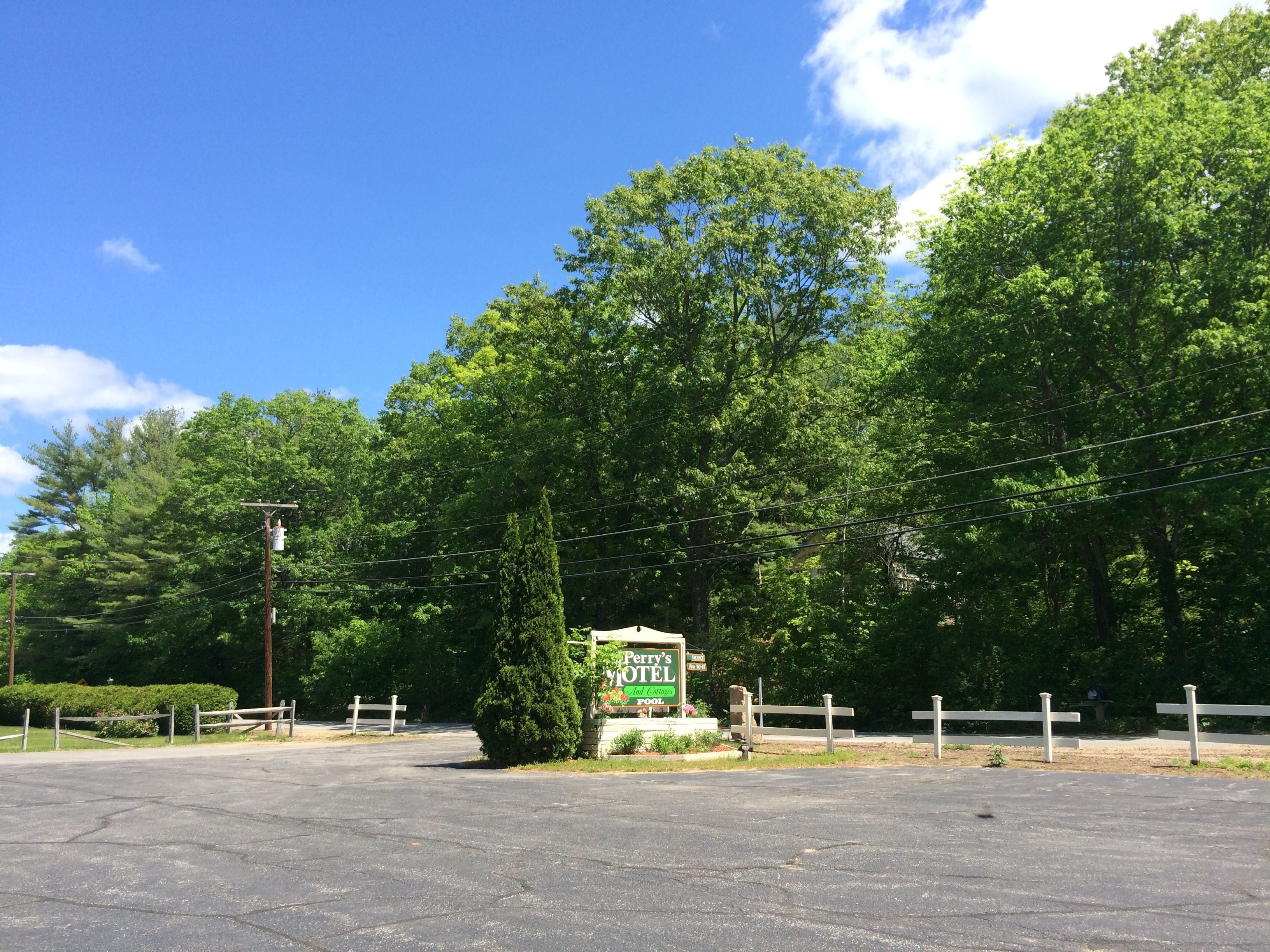 Un parking avec un panneau indiquant le « Perry’s Motel », entouré d’arbres et sous un ciel dégagé.
