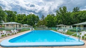 En rektangulær swimmingpool med blå kant, omgivet af hvide stole og et hegn.