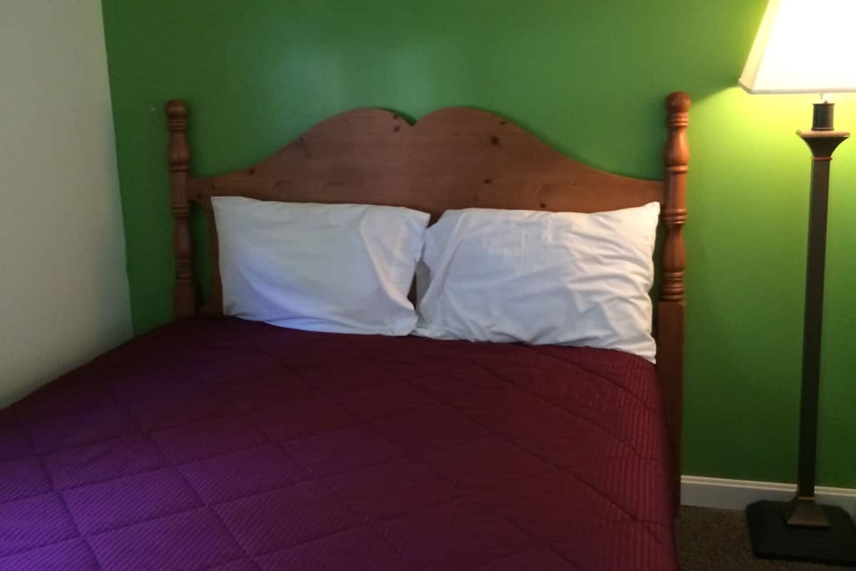 Uma cama com cabeceira de madeira, duas almofadas brancas e um edredom acolchoado roxo.