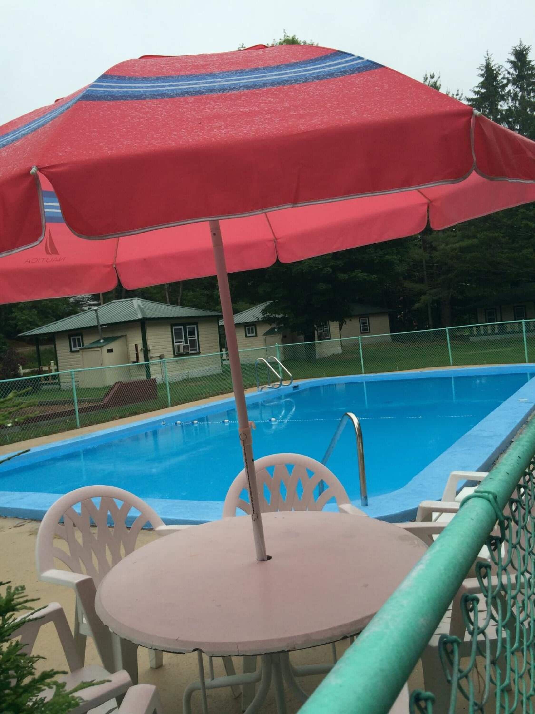Un área junto a la piscina con una sombrilla roja, una mesa redonda y sillas blancas.