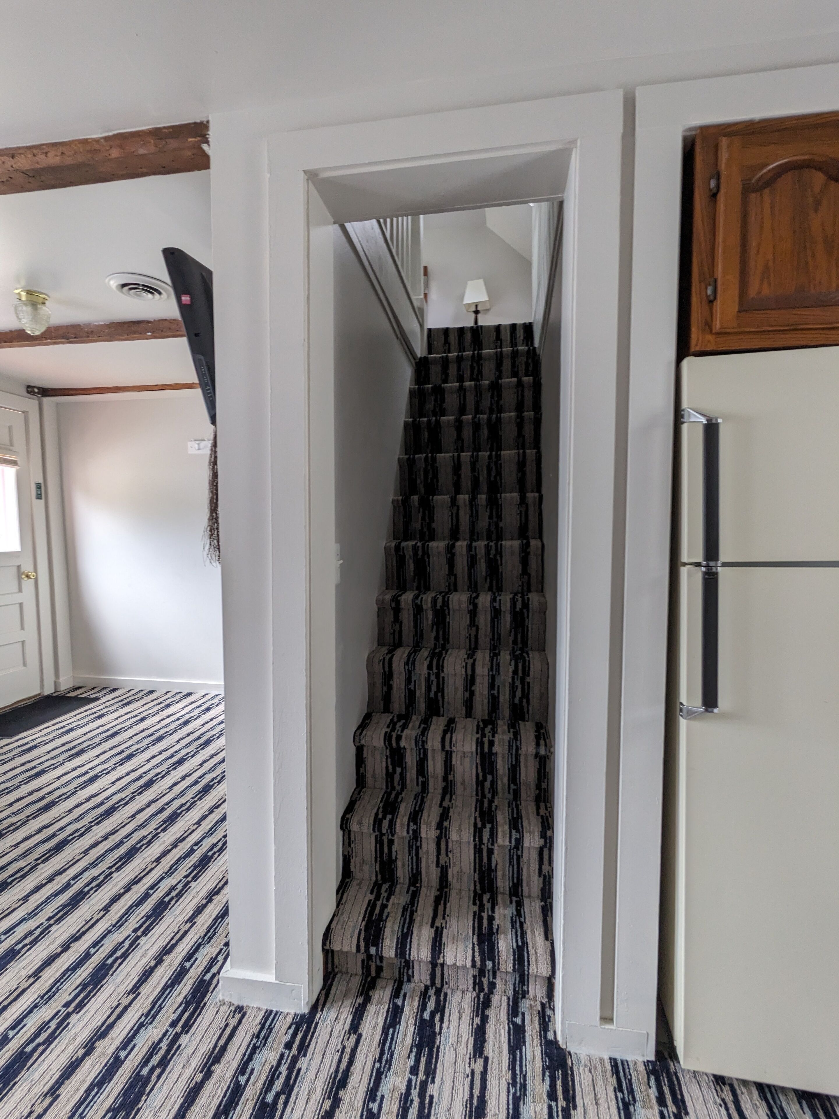 A staircase with striped carpeting leading to a landing, a white refrigerator, and a wooden cabinet.