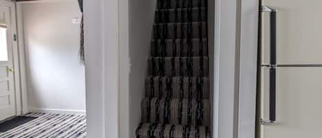 A staircase with striped carpeting leading to a landing, a white refrigerator, and a wooden cabinet.