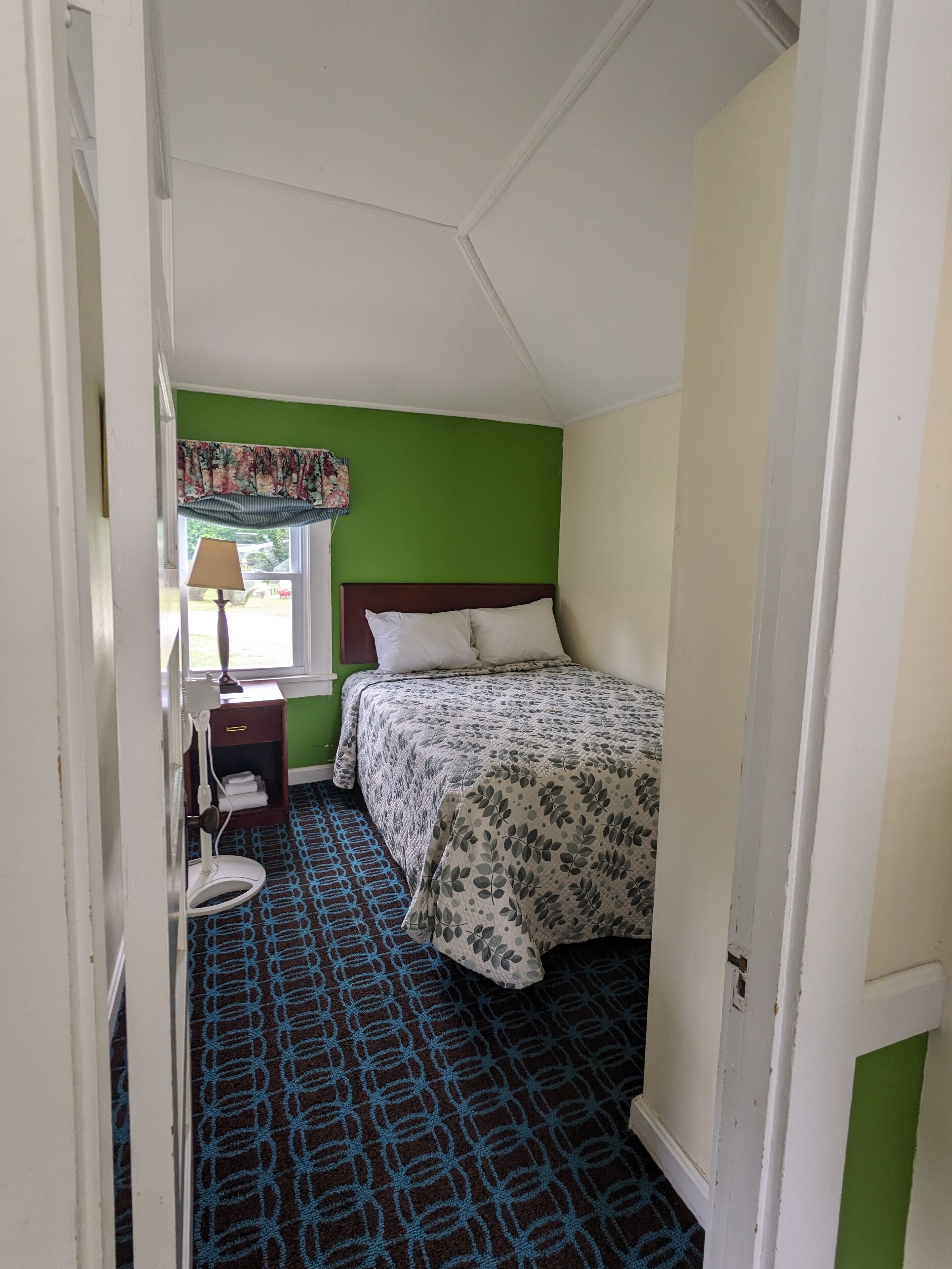 A small, single-bed room with a green accent wall, a patterned floor, and a window with a floral valance.