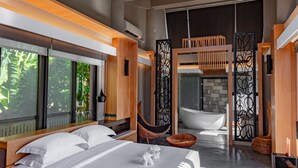 Un dormitorio moderno con una cama grande, un banco de madera, una bañera y vistas a zonas verdes.