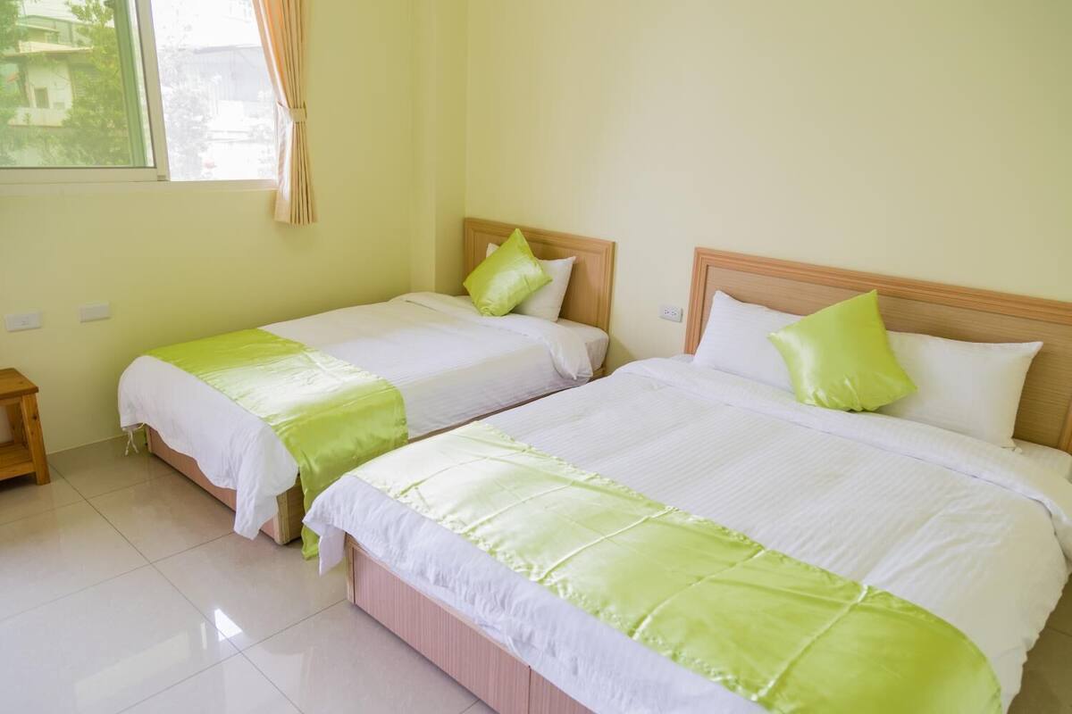 Habitación de hotel con dos camas, cada una con cabecero de madera y ropa de cama verde y blanca.