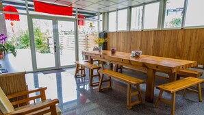 Un comedor de madera con bancos y una mesa, ventanas amplias y vistas al exterior.