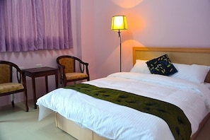 A neatly made bed with white linens and a green throw, a bedside lamp, two wooden chairs, and a small table. - Just Stay (Yuanshan)