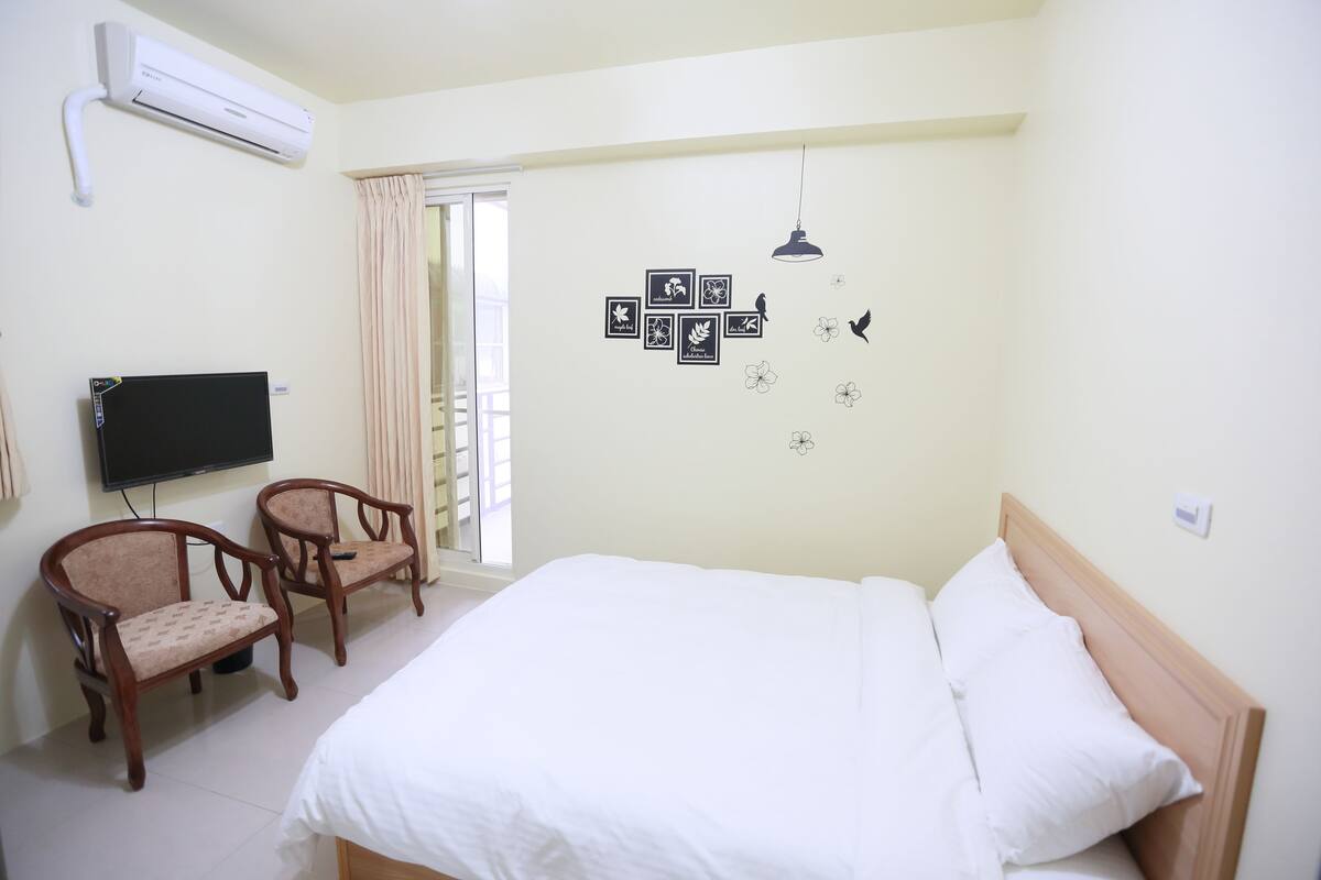 Un dormitorio con una cama, dos sillas, un televisor y un aire acondicionado instalado en la pared.