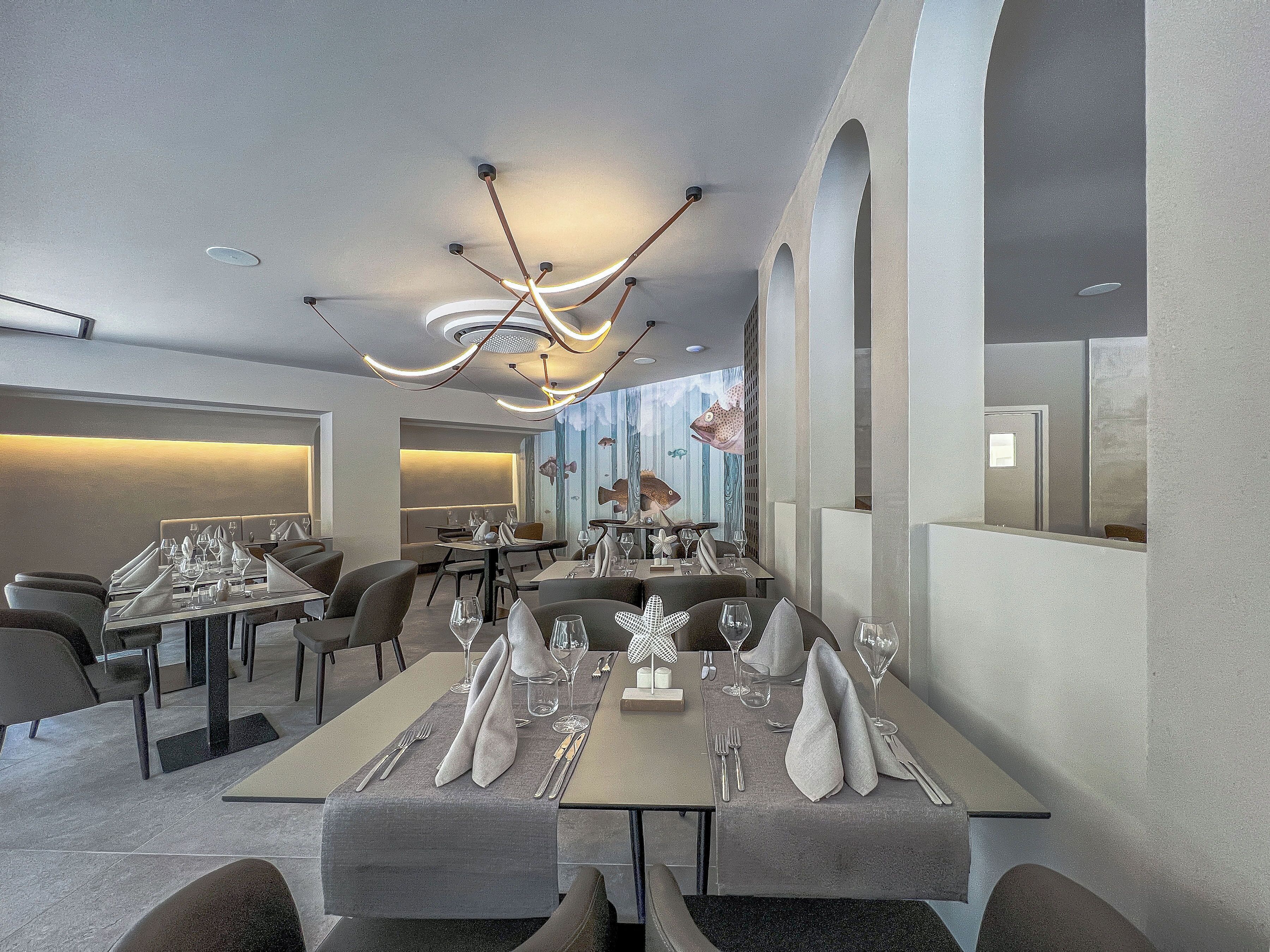 A modern restaurant interior with high ceilings, contemporary lighting fixtures, and a long dining table set for a meal.