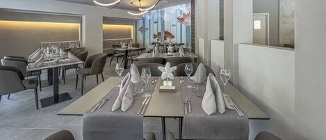 A modern restaurant interior with high ceilings, contemporary lighting fixtures, and a long dining table set for a meal.