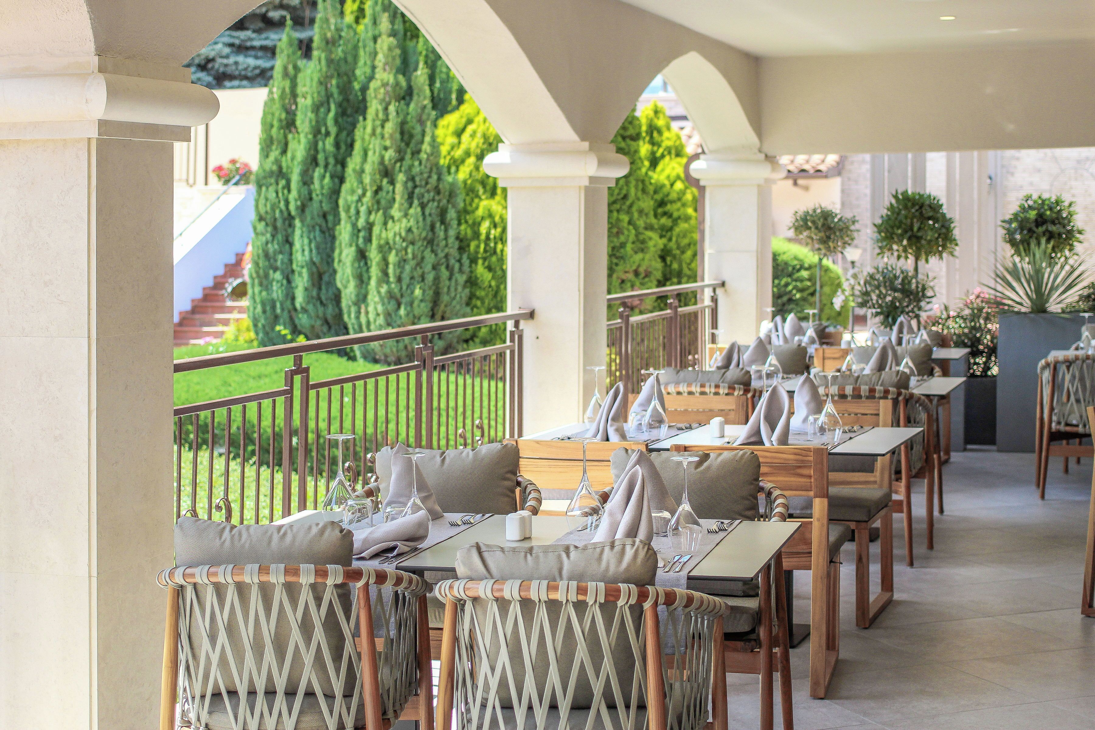 An outdoor dining area with tables and chairs, a staircase, and greenery in the background.