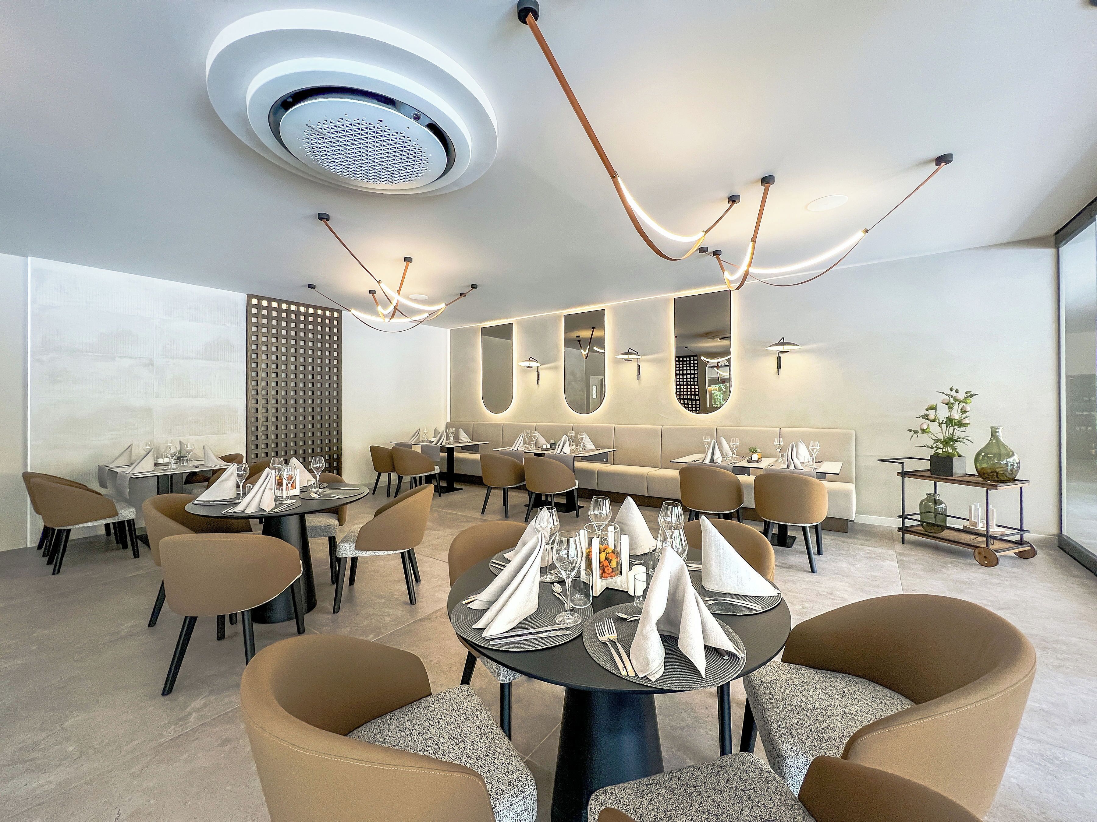 A modern dining area with round tables, cushioned chairs, and contemporary lighting fixtures.