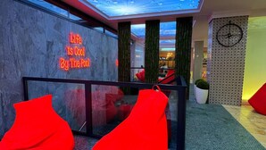 A modern lobby with a ceiling that simulates raindrops, a neon sign stating "Life is Cool By The Pool," and red seating areas.
