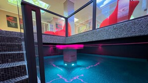 Una piscina interior moderna con un diseño único, que presenta un pilar central y detalles de iluminación en rosa.