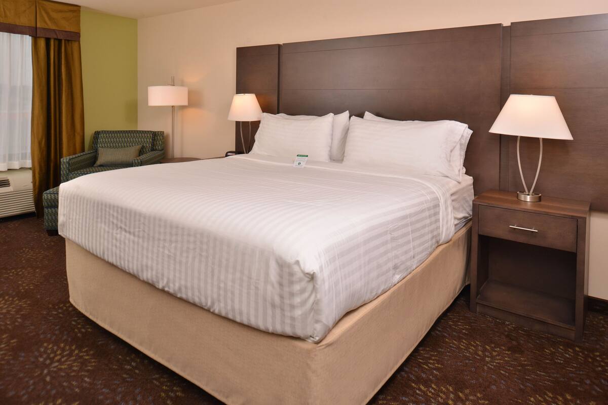A hotel room with a large bed, two bedside lamps, a chair, and a nightstand.