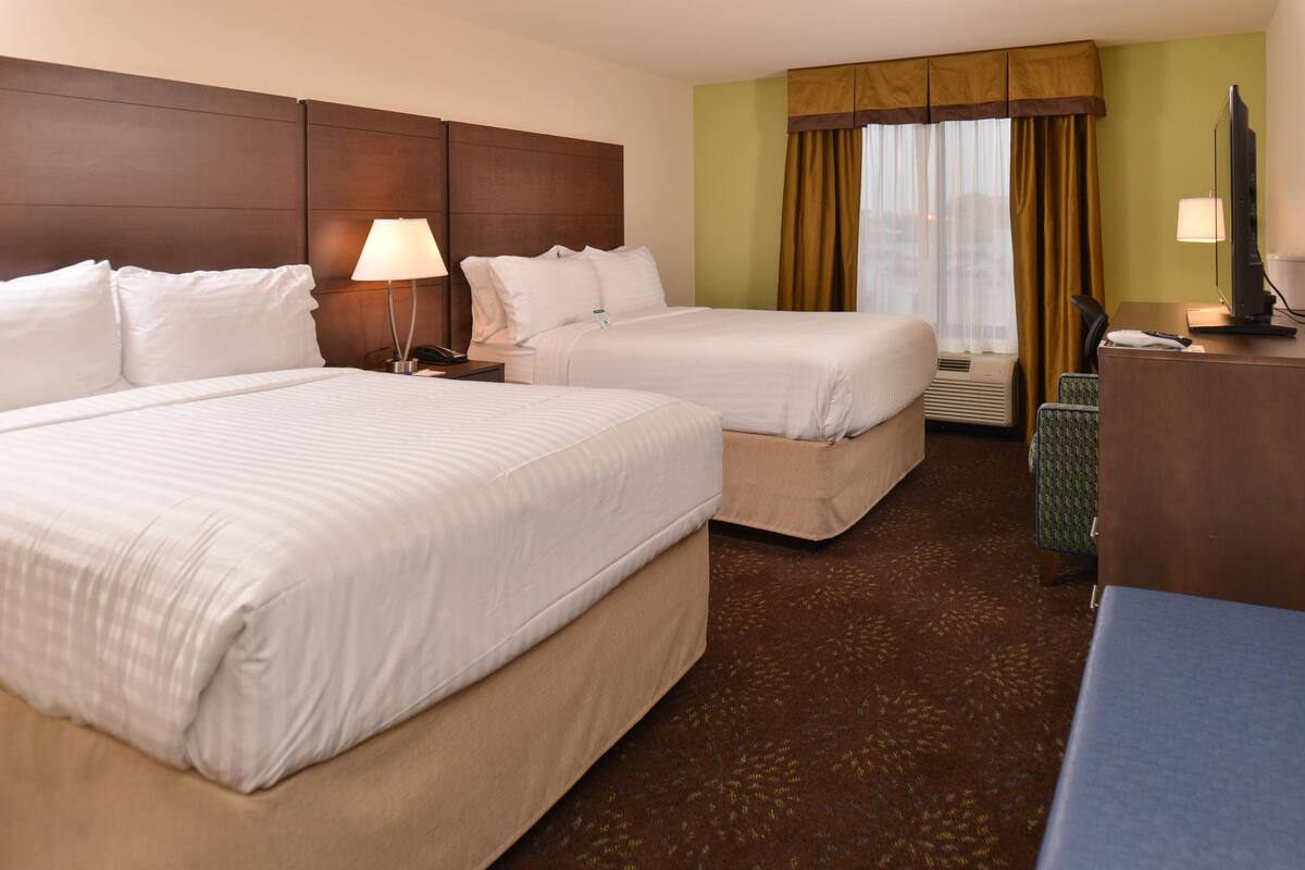 A hotel room with two beds, a desk, a chair, a television, and a window with curtains.