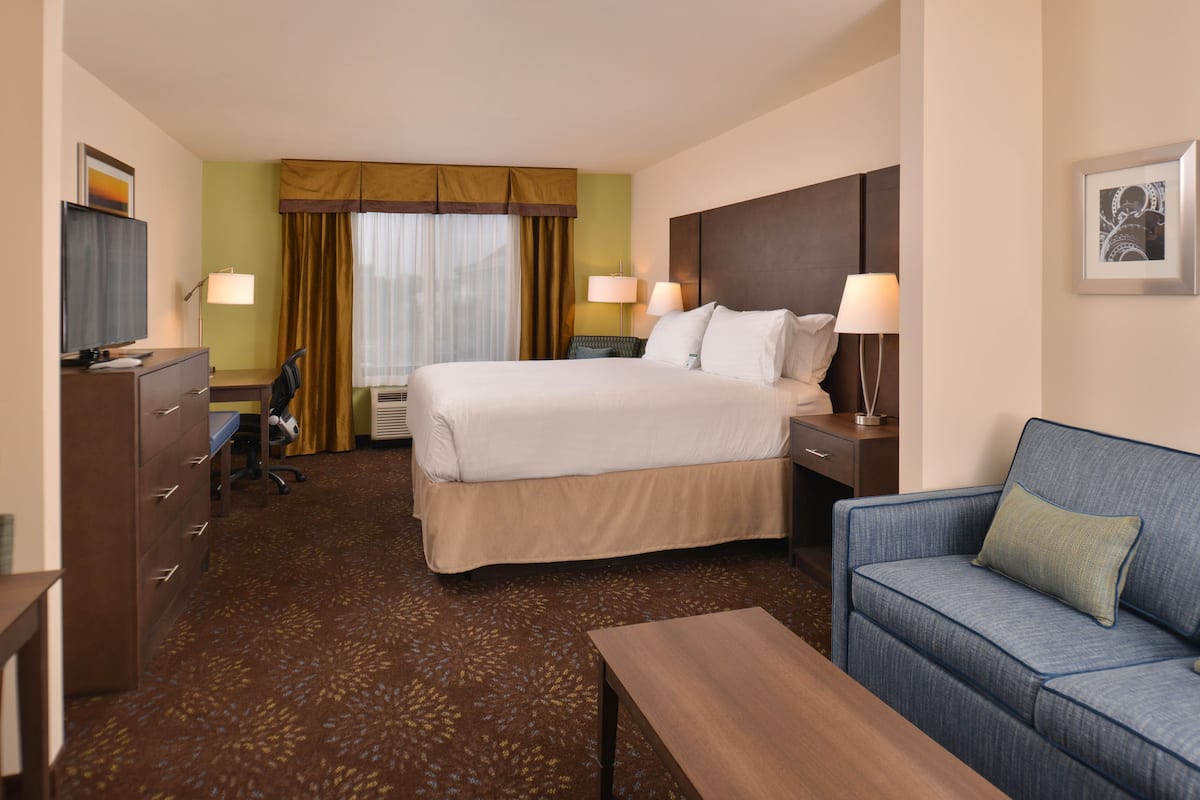 A hotel room with a large bed, a sofa, a desk, a chair, and a TV.