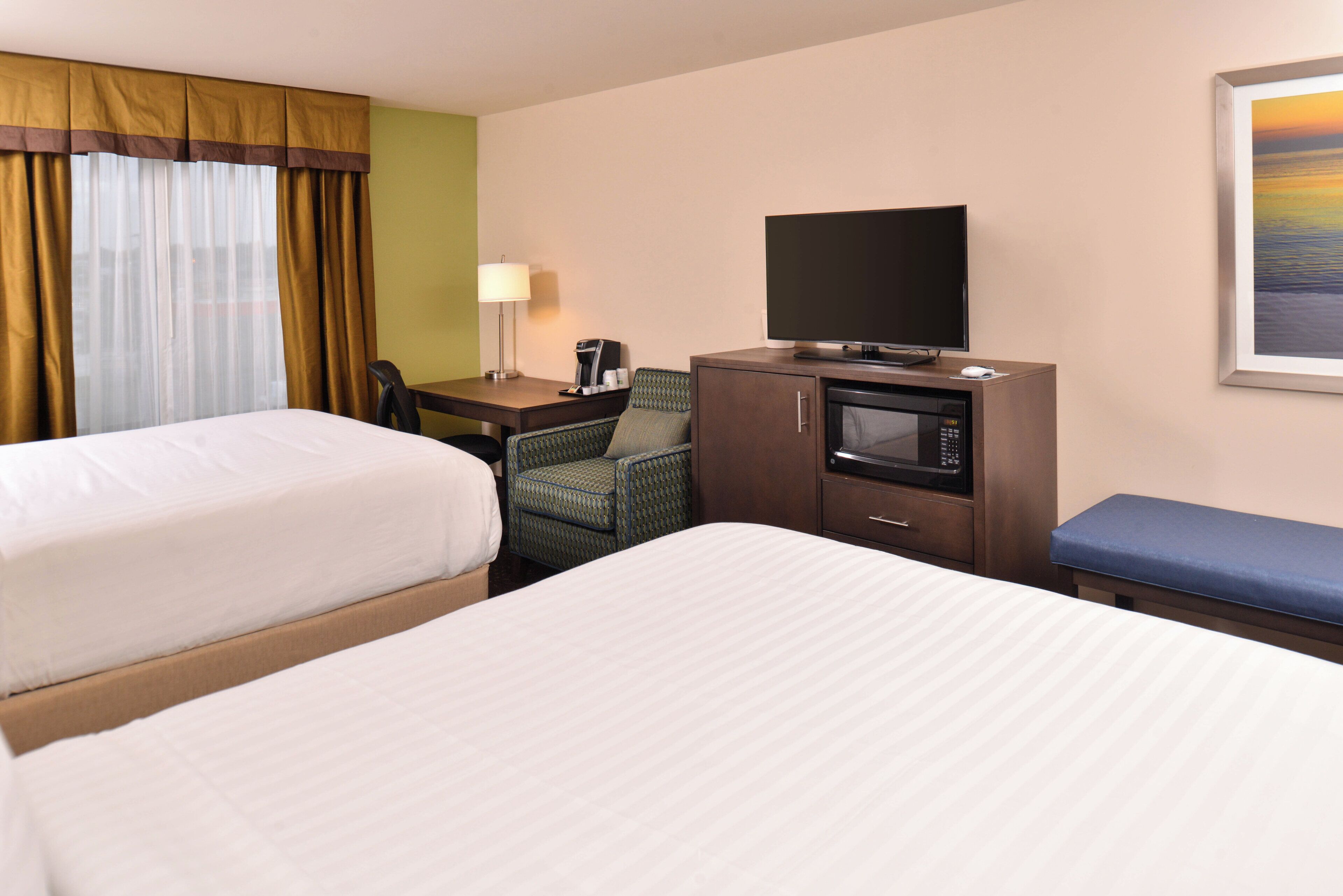 Une chambre d’hôtel avec deux lits, un bureau avec un ordinateur, une télévision, un four à micro-ondes et une chaise.
