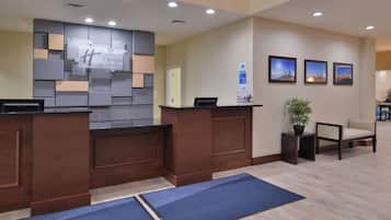 A reception area with a wooden reception desk, a wall-mounted sign, a potted plant, and framed artwork on the wall.
