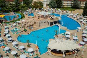 Une grande piscine extérieure entourée de chaises longues et de parasols, agrémentée d’une petite cascade et d’une formation rocheuse.