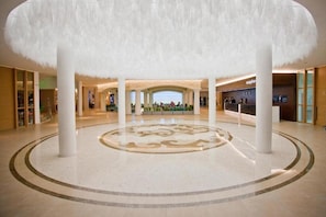 Eine gerĂ€umige Lobby mit einem zentralen, kreisförmigen Design, weiĂen SĂ€ulen und einem Empfangsbereich im Hintergrund.