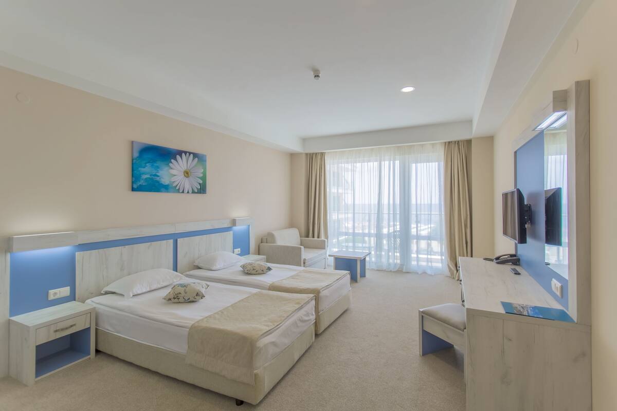 A hotel room with two beds, a desk, a chair, a TV, and a painting on the wall.
