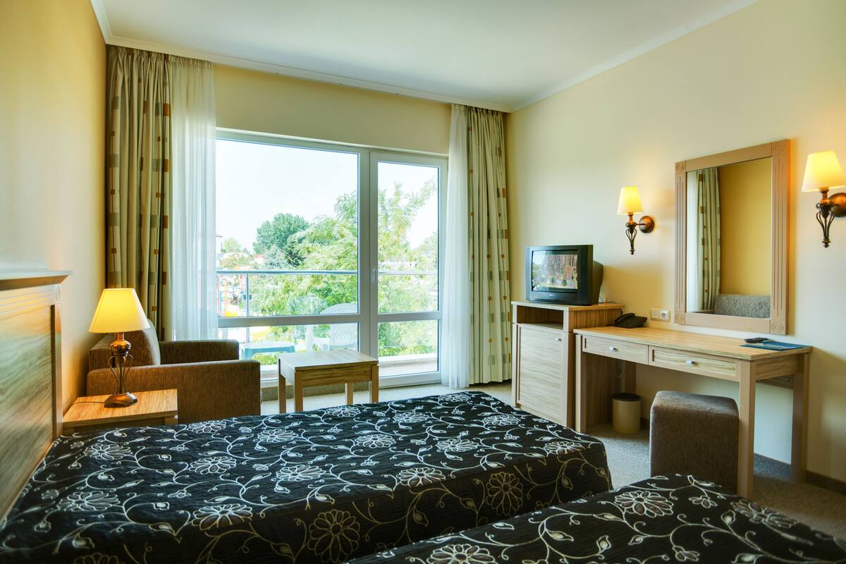 A hotel room with a bed, a desk, a chair, a television, and a window with curtains.