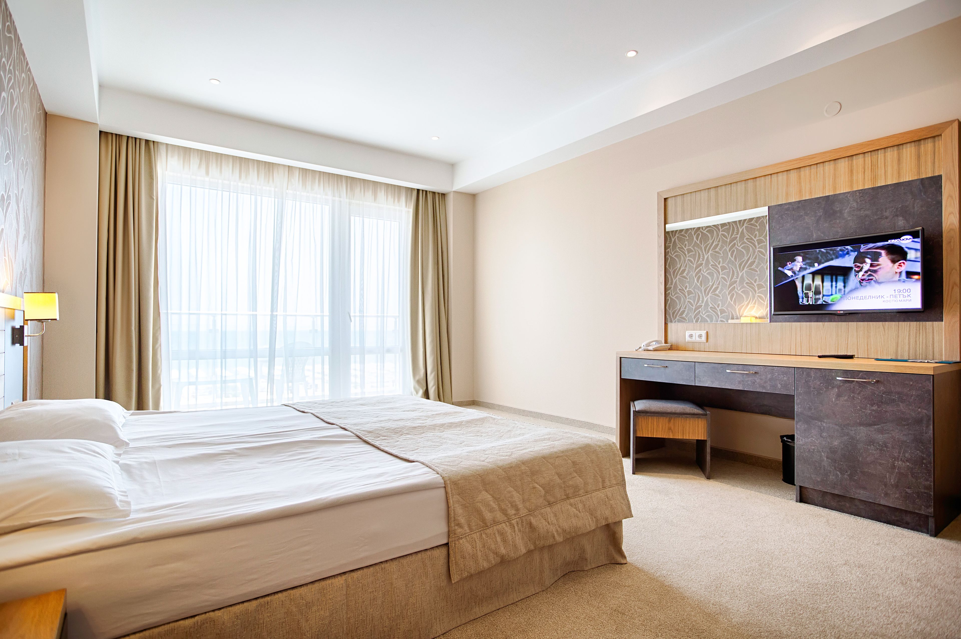 A hotel room with a bed, a desk, a chair, a television, and a window with curtains.